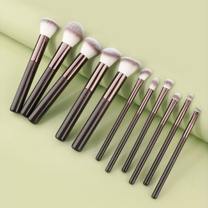 The Technique PRO Chocolate Bronze Makeup Brush Set features 11 professional brushes with dark handles and white-tipped bristles, neatly arranged on a light green background for all your makeup application needs.