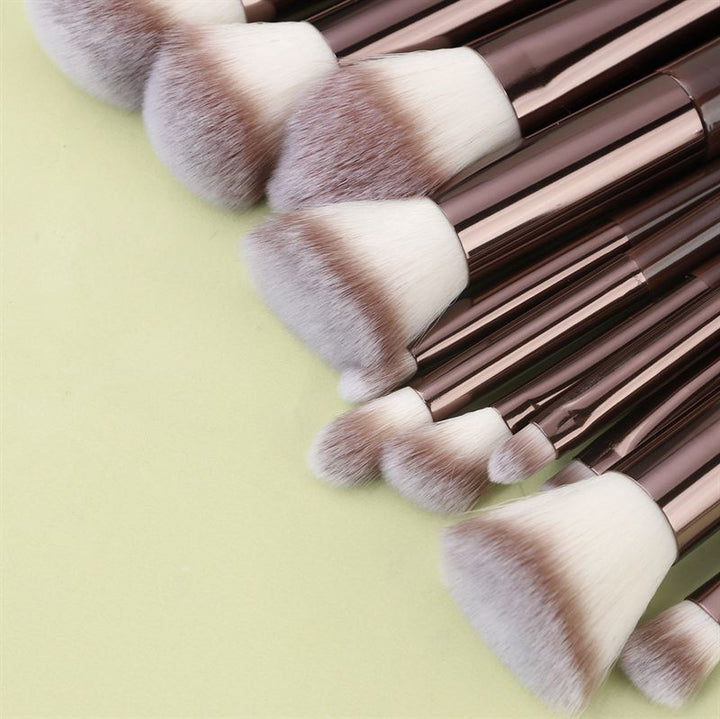 The Technique PRO Chocolate Bronze Makeup Brush Set (11 pieces) features brown handles and soft white bristles, stylishly displayed on a light green surface.